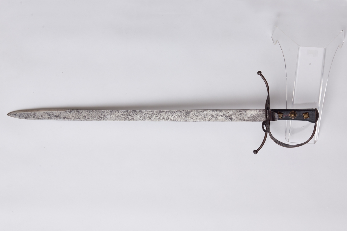 Sabel a): Klingen hulslipt til 17,5 cm fra spissen. Ryggen er tynnslipt fra spissen og 17 cm. oppover. Grepets plate, bøyle og knapp er støpt av messing. Kavlen er av presset horn med rifler hvori metallbånd. Dekorert.
