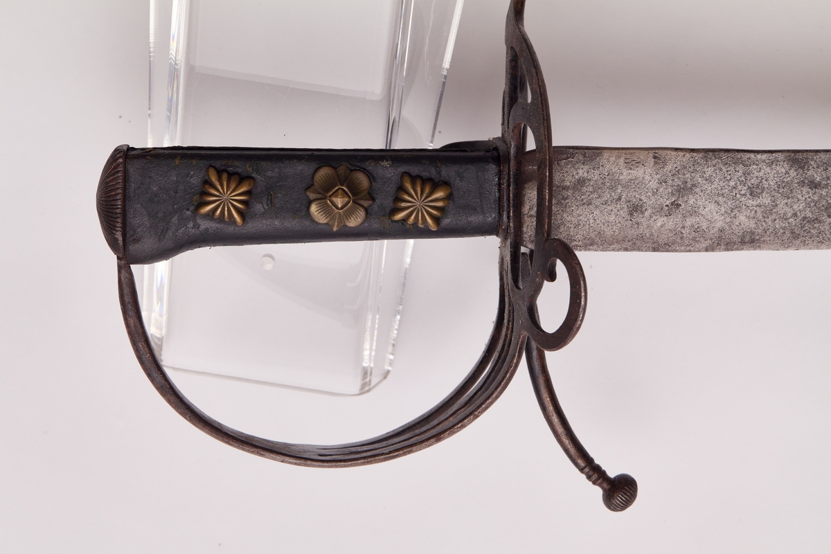 Sabel a): Klingen hulslipt til 17,5 cm fra spissen. Ryggen er tynnslipt fra spissen og 17 cm. oppover. Grepets plate, bøyle og knapp er støpt av messing. Kavlen er av presset horn med rifler hvori metallbånd. Dekorert.