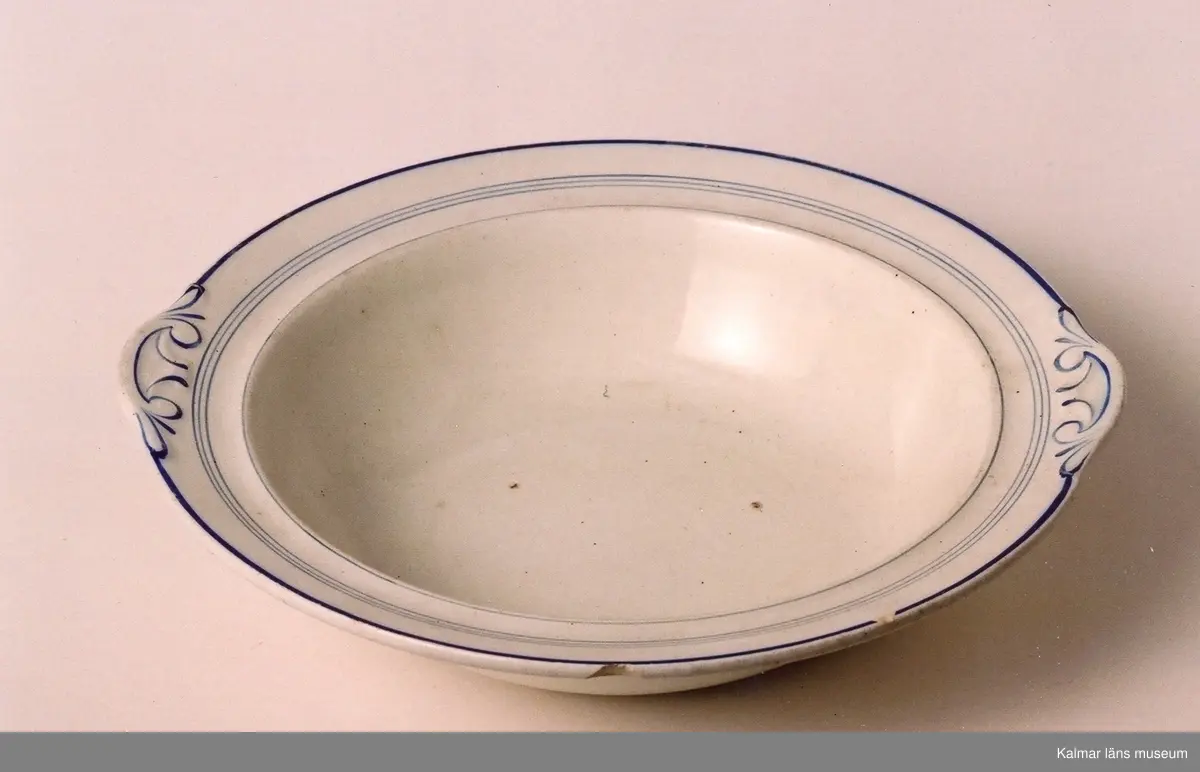 KLM 39615:1-2. Tallrikar, djupa, 2 stycken. Diam 22,5 cm, största diam vid dekor 23,6 cm, H 5 cm. Vitt porslin med blå dekorränder, dekor på brättet som förtydligar karaktären av greppen. Stämpel: inpressad: JL Rörstrand AD 9 z13.