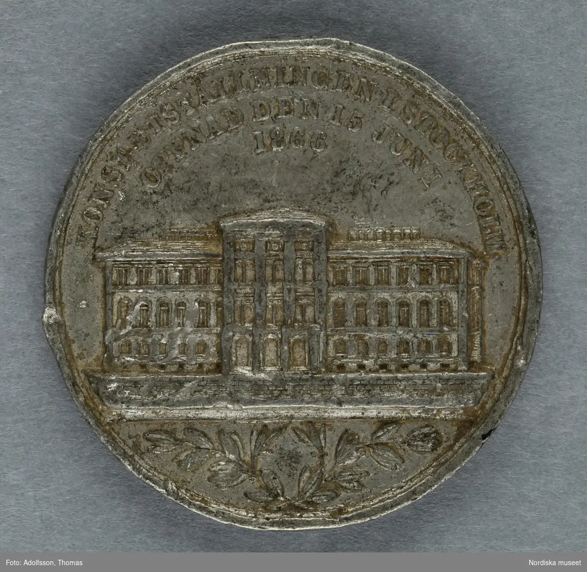 Huvudliggaren:
"Minnespenning. Å ena sidan: 'INDUSTRIUTSTÄLLNINGEN I STOCKHOLM/SEDD FRÅN SYDVESTRA SIDAN/ÖPPNAD DEN 15 JUNI 1866'. Å den andra sidan: 'KONSTUTSTÄLLNINGEN I STOCKHOLM ÖPPNAD DEN 15 JUNI 1866'. Genom byte med antikvitetshandlaren A.G. Hagander i Stockholm. Ankom 19/9 1888."
