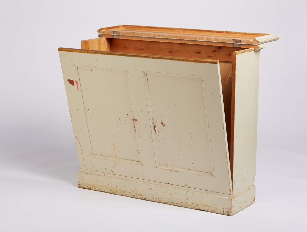Et gulvskap der topp-platen har hengsler og kan løftes opp. Frontplaten har også hengsler og kan felles forover. Frontplaten blir holdt igjen av to messingkjeder. Frontplaten har 2 speil (fyllinger). Bakplaten er skrådd.