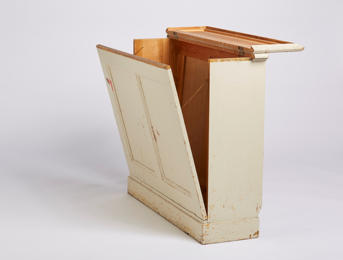 Et gulvskap der topp-platen har hengsler og kan løftes opp. Frontplaten har også hengsler og kan felles forover. Frontplaten blir holdt igjen av to messingkjeder. Frontplaten har 2 speil (fyllinger). Bakplaten er skrådd.