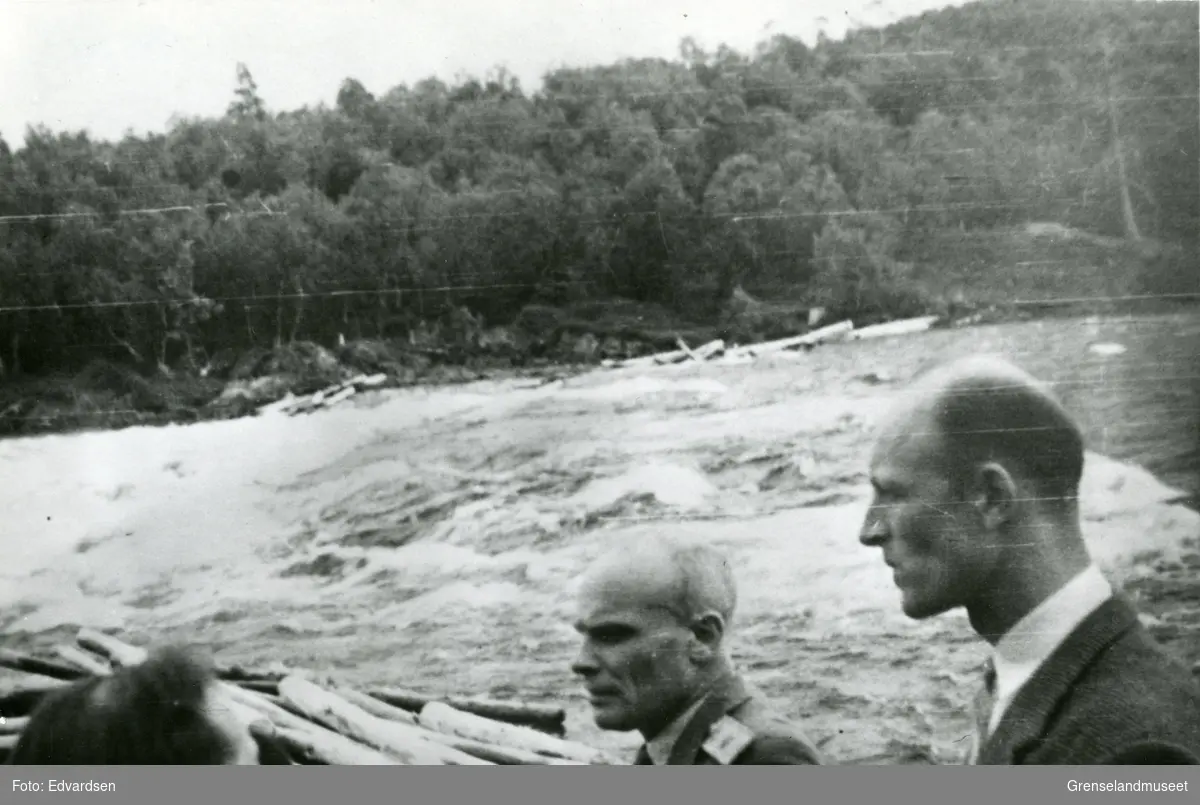 Grenseoppgang? Skogfossen med tømmer. I forgrunn står tre menn, den midterste med uniform. 