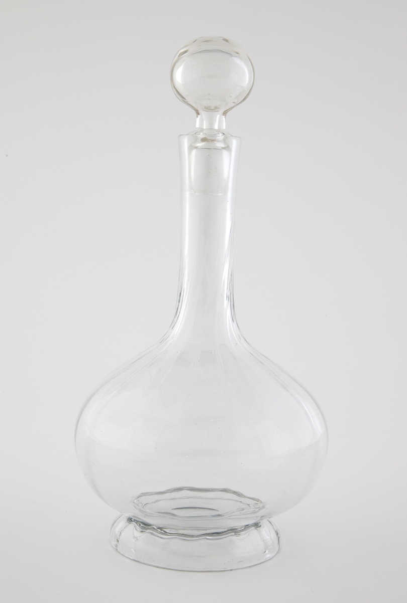 Glasskaraffel med propp i klart glass. Korpus er kuleformet med en lang og slank hals. Karaffelens riller snor seg fra korpus og oppover halsen.