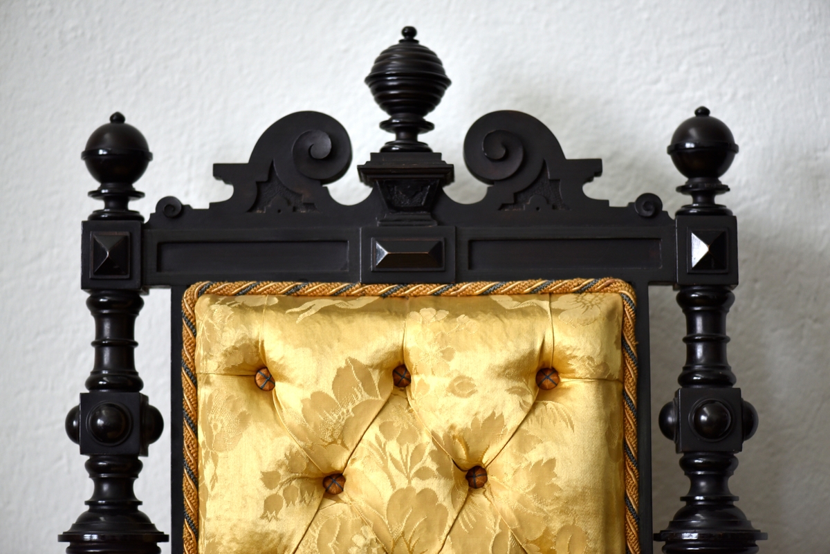 Stol i nyrenässansstil tillverkad av svart päronträ och klädd i gul sidendamast. 
Sargen och ryggstödsramen är rikt utsnidade. Det främre benparet är svarvade och försedda med trissor. Det bakre benparet är skurna, något svängda och bakåtlutande. 
Den stoppade sitsen och ryggbrickan är klädda med ett gult sidendamasttyg med invävt mönster i form av blommor, blad och band bland annat. Ryggbrickan är försedd med 13 klädda knappar.
Runt klädselns kanter mot ramverket sitter ett tvinnat kantband i gult, vitt och blått.