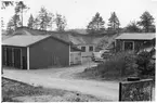 Vägstation Vmo B2, Knutby. Åsby grusgrop. Förrådsbyggnad, på planen uppställd stubbrytare (stenbrytare). Volvo PV 444. Upplag av bränslefat. Skylt 