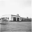 Vägstation C1, Enköping. Huvudbyggnad, med från vänster; verkstadsdel, kontorsdel, garagedel. Personbilar parkerade vid gaveln.