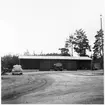 Vägstation E10, Östra Husby. Garage- och förrådsbyggnad. Personbil, E10304, framför byggnaden. Luttunna på vagn, plogar till vänster.