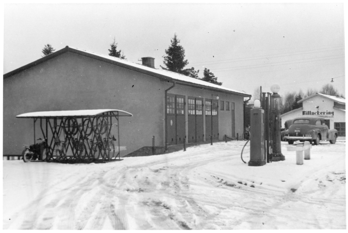 Vägstation F3, Smålandsstenar. Garagebyggnad. Cykelställ med cyklar vid gaveln. Bensinpumpar (drivmedelspumpar). Personbil med skylt "Tjänstebil". I bakgrunden byggnad med texten "Billackering". 