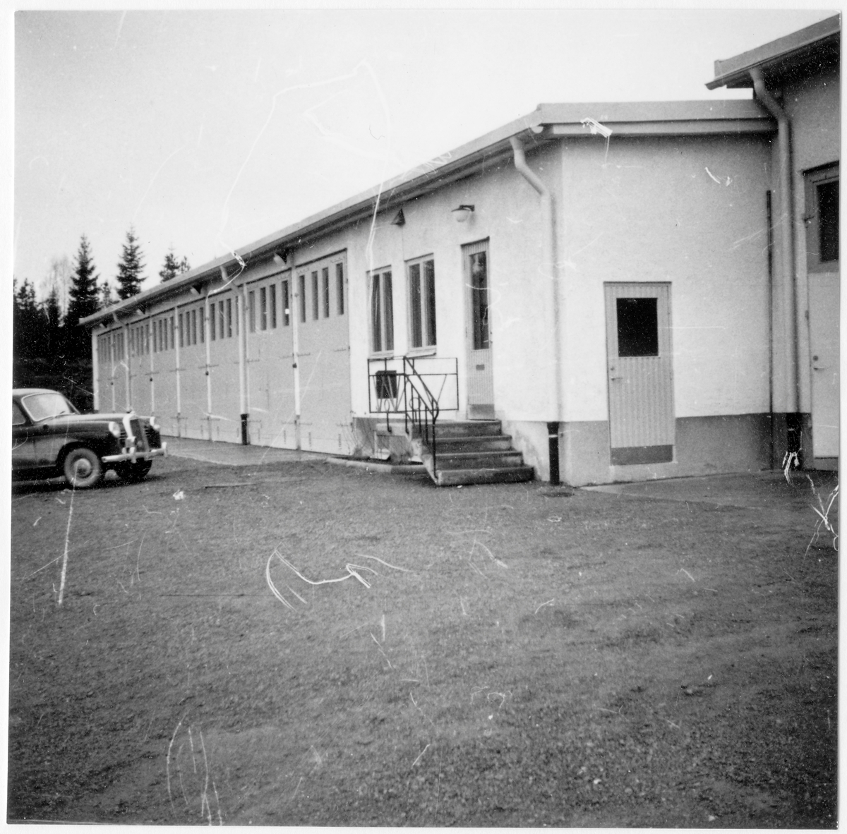 Vägstation G10, Åseda. Vägstationens huvudbyggnad med garagelänga och kontorsdel. Trappräcket till kontorsdelen med smidda inlägg "VoV" (Väg- och vattenbyggnadsstyrelsen). Personbil Mercedes skymtar till vänster.