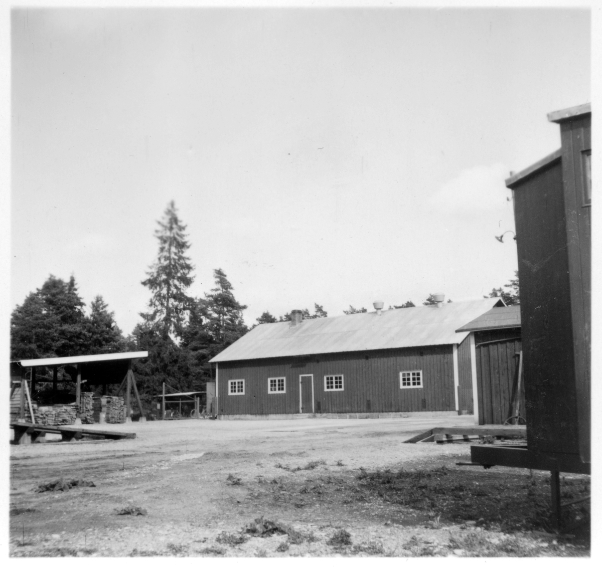 Vägstation I5, Stånga. Baksidan av garagebyggnaden. Diverse materialupplag.  Manskapsvagn ÅSA transportabla manskapsbod, Åmåls Sågverks AB, skymtar till höger.