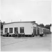 Vägstation K1, Lyckeby. Vägstationens huvudbyggnad med från vänster verkstadsdel, kontorsdel, garagedel. Diverse material upplagt vid gavel av verkstaden.