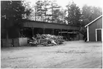 Vägstation N1, Hov. Öppen förrådsbyggnad. Upplag av ved framför.