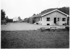 Vägstation O4, Henån. Vägstationens huvudbyggnad med kontorsdel närmast och garage. På garageplan en stenkross. I förgrunden en vägsladd. Bensinpump (drivmedelspump).