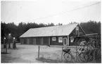 Vägstation P13, Brålanda. Garage- och förrådsbyggnad. Cykelställ med cyklar, bensinpumpar (drivmedelspumpar), sidoplogar, spetsplogar, personbil Volvo PV. Lågt nätstängsel.