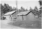 Vägstation S1, Kristinehamn, filial Backa.  Garagebyggnad och förrådsbyggnad. Lastbil framför garagebyggnaden. Fem manspersoner och en motorcykel vid gaveln. Invid väg med skylt för busshållplats, med texten 