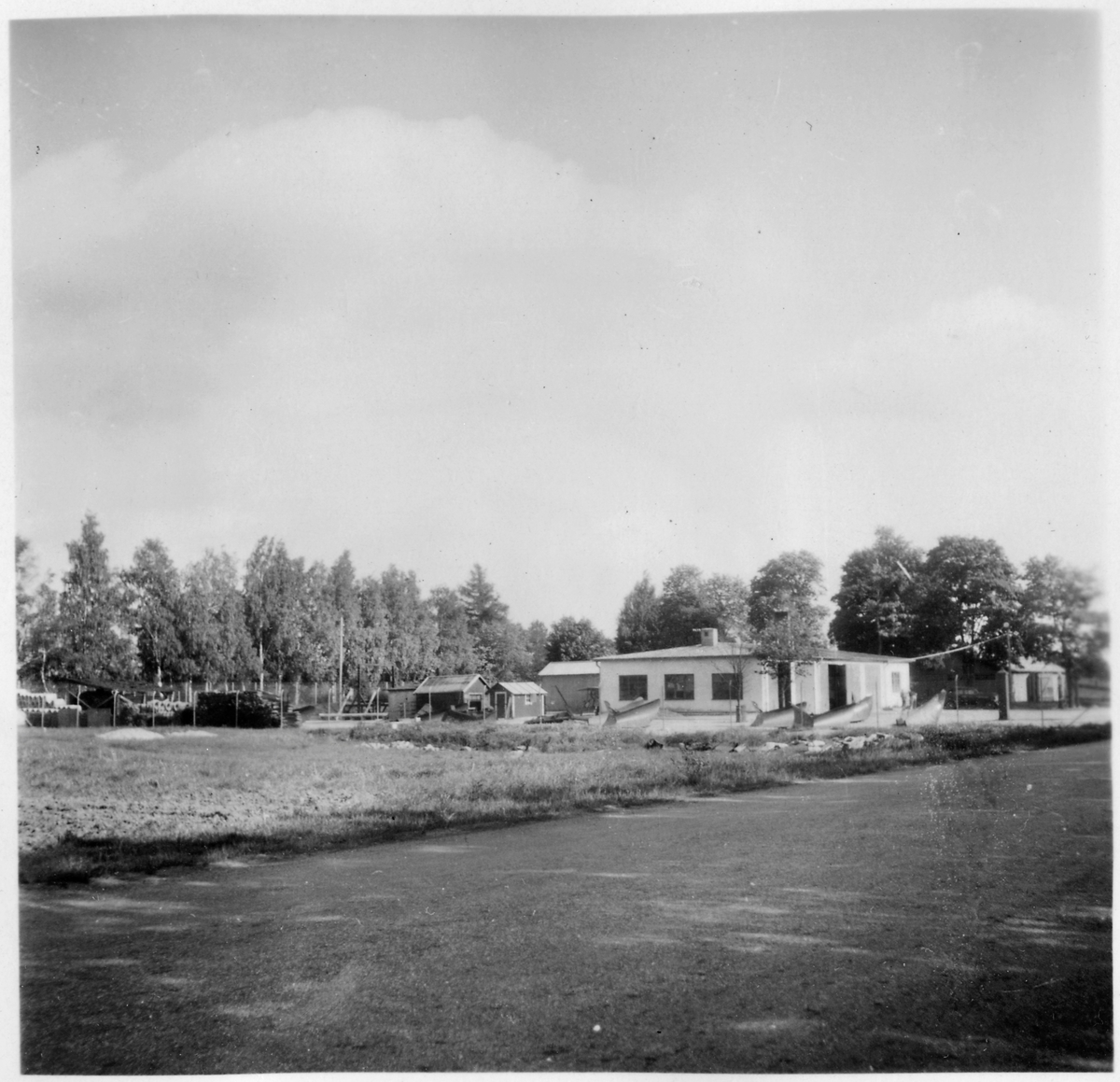 Vägstation T3, Hallsberg. Vy mot vägstationen med garagebyggnaden, med kontor i bortre delen av byggnaden, till höger och olika mindre förrådsbyggnader. Nätstängsel runt anläggningen. Spetsplogar och sidoplogar uppställda på garageplan. Invid väg.