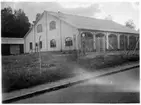 Vägstation W2, Hedemora. Garagebyggnad. Tegelbyggnad, troligen före detta industrilokal. Bensinpump (drivmedelspump) Ljungmans, modell Vici. Förrådsbyggnad i bakgrunden. Stängsel runt anläggningen. Invid gata.