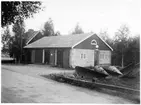 Vägstation W9, Nås, filial Dala-Järna. Garagebyggnad, delvis murad. Vid gaveln bensinpump (drivmedelspump), spetsplogar och sidoplogar. Invid väg, med vägräcke med navföljare av plank och wire mellan stenstolparna. Bostadshus i bakgrunden.