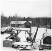 VFW, Depåförråd (Vmo W6). Vy över garageplan. Förrådsbyggnad och smedja i bakgrunden. Diverse olika väghållningsmaskiner och fordon, bland annat schaktmaskin (under presenning på flak), lastbil, bränsletank (