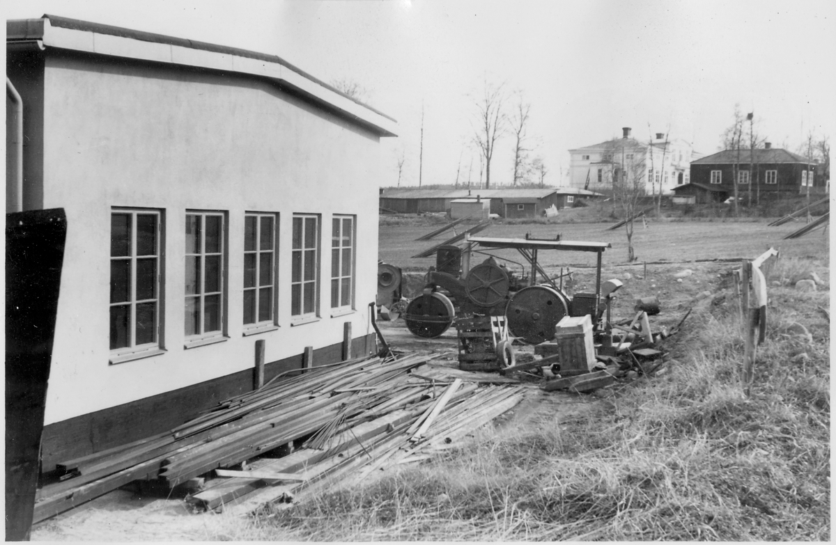 Vägstation Y6, Älandsbro. Baksidan av garagebyggnaden. Diverse material, "skrot", motorvält Munktell. Bostadshus i bakgrunden. Eventuellt depåverkstadens (länsverkstadens) material.