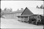 Vägstation AC1, Nordmaling. Vägstationens huvudbyggnad med (från vänster) verkstad, kontor och garage. Förrådsbyggnad i förgrunden. Upplag av diverse materiel, bland annat slangar, bränslefat. Vägmärke 