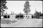 Vägstation AC8, Burträsk. Vägstationens huvudbyggnad med garage, kontor och förråd. Avstängningsbockar framför de öppna garageportarna. Invid väg med vägvisare, tre stycken på stolpe svart/gul märkning. Trehjuling (barncykel) vid vägkanten.