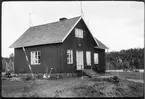 Vägstation AC12, Norsjö. Färjvaktarbostad vid Arnbergssundet. Bostadshus för färjvaktaren. Färjleden över Arnbergssundet i bakgrunden. Kvinna som arbetar i trädgården.