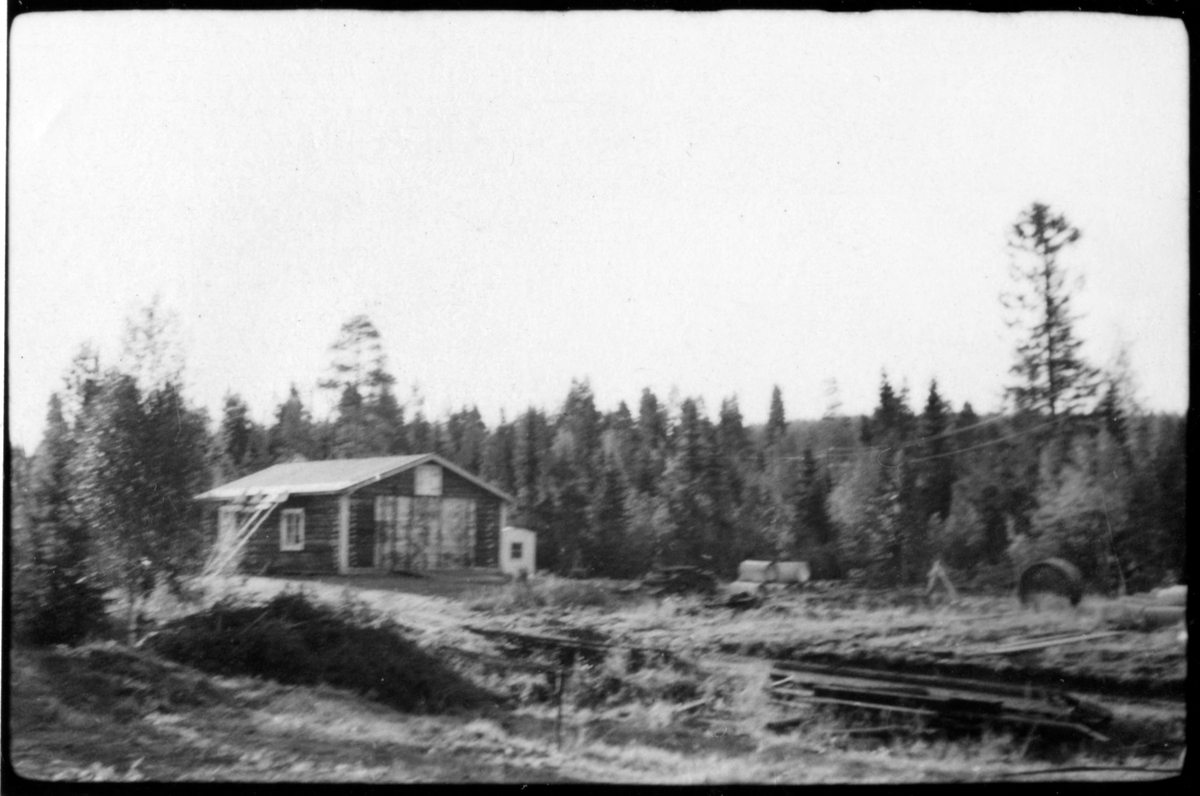 Vägstation AC19, Storuman. Garagebyggnad, i skogsområde. Vägmärken lutade mot byggnaden.