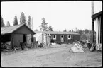 Vägstation AC19, Storuman. Förrådsbyggnad och eventuell manskapsbod. Framför förrådsbyggnaden fältässja och ambolt, vägmärken lutade mot byggnaderna, skottkärror.