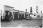 Vägstation BD12, Korpilombolo. Vägstationens huvudbyggnad med verkstad, kontor och garage. Personbil på garageplan. Förrådsbyggnad i bakgrunden.