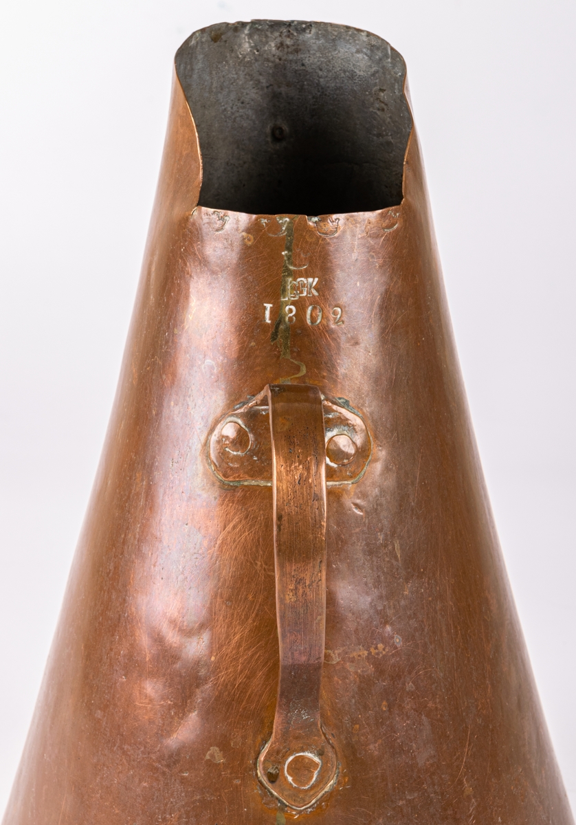 Brännvinsmått, av koppar, konisk form, ett handtag. Krönt 1802, "GK".