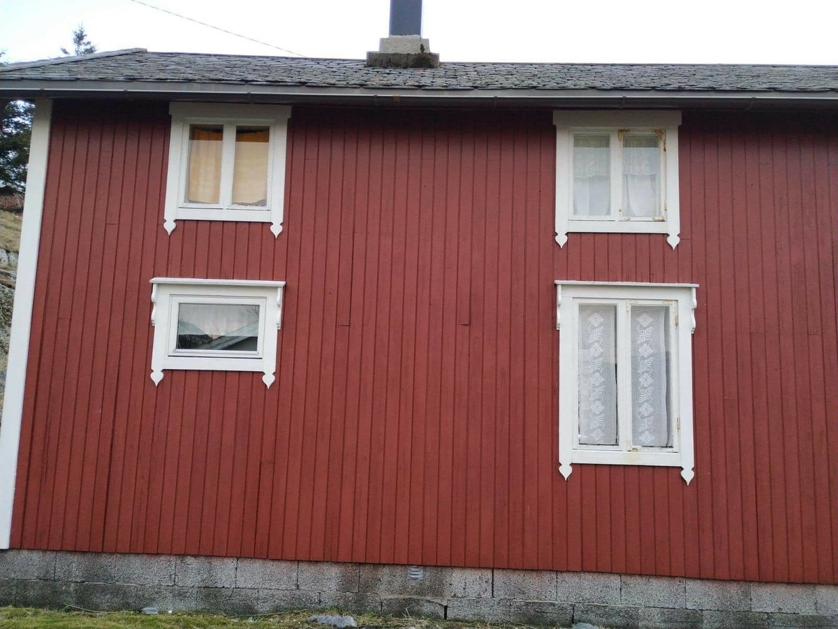 Huset har panel stående panel, malt rødt med hvit dekor på og rundt vinduer. Skifertak.