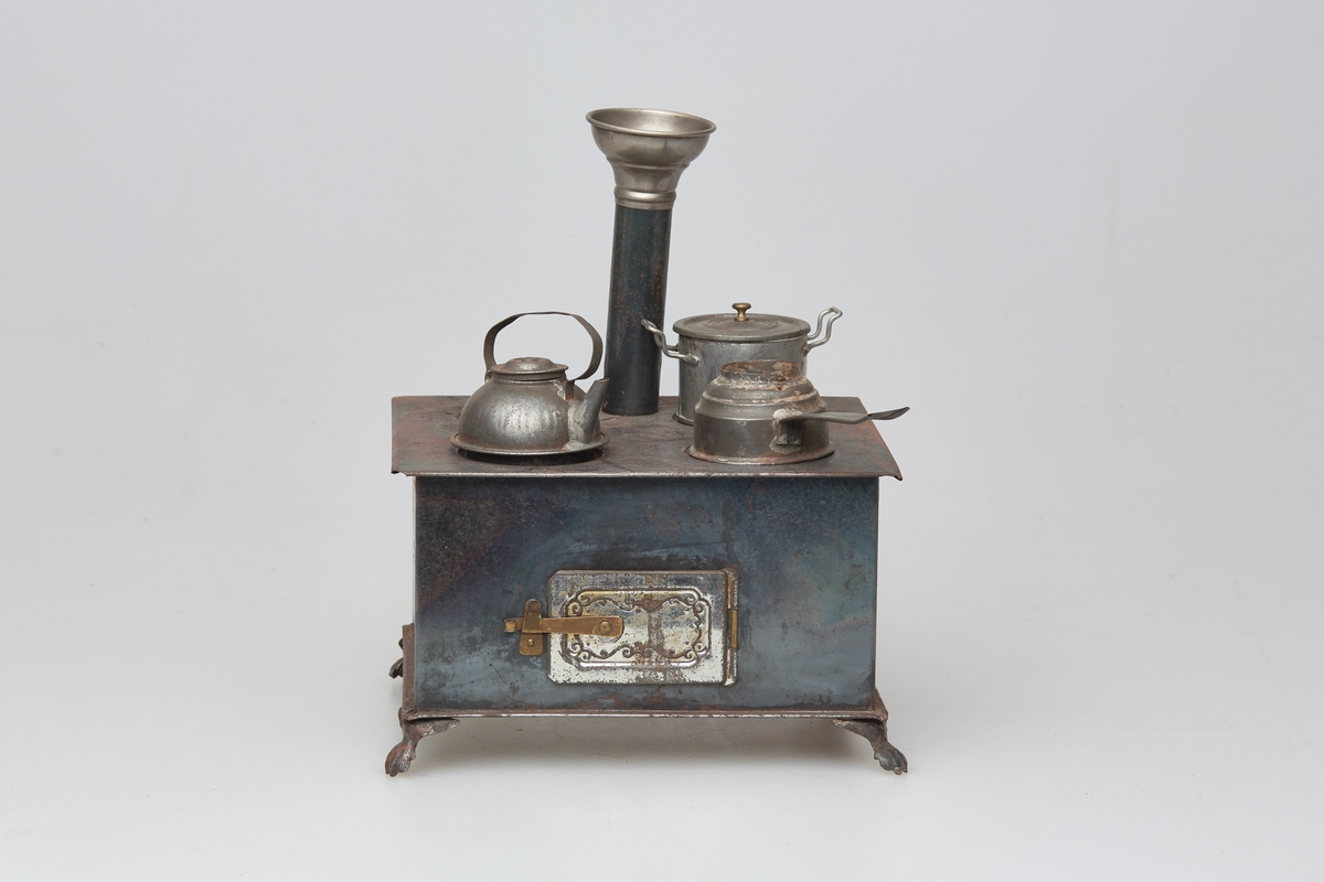 Lekekjøkken med komfyr (a) med to kjeler (b og c) med lokk, steikepanne (d), kaffekjel (e), og trolig brenner (f) til komfyren. Laget av blikk og messing.