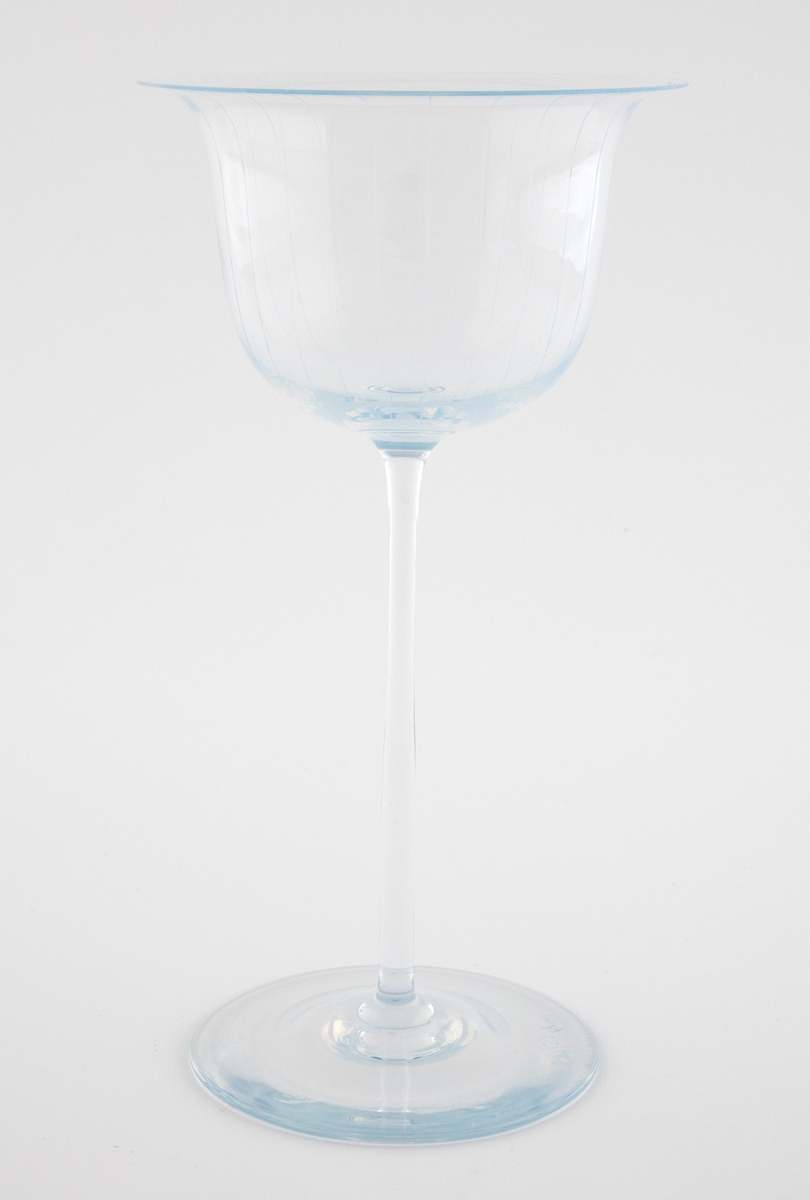Alterkalk i gjennomskinnelig glass med opaliserende partier. Klokkeformet kupa med bred munning, som hviler på en høy og smal stett og sirkulær fotskive. Kupa er dekorert graverte vertikale linjer.