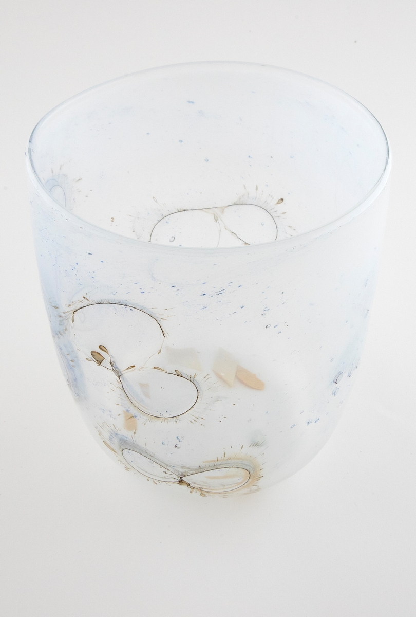 Sylinderformet glassbolle. Bunn og nedre del av korpus er utført i klart glass, mens øvre del domineres av melkehvitt halvgjennomskinnelig glass. Innlagte metalltråder danner åttetalls- og halvsirkelformede elementer på korpus. I glasset er det en rekke luftblærer i ulike størrelser, samt dråpeformede spetter i blått og brunt. Puntemerke under bollens bunn.
