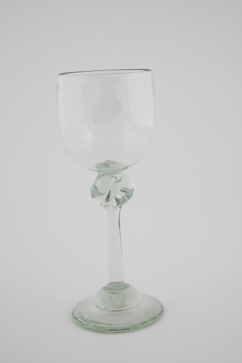 Drikkeglass i klart grønntonet glass med klokkeformet kupa, som hviler på en tynn stett med spiralformet vulst. Rund fotplate, noe opphøyet i midten.