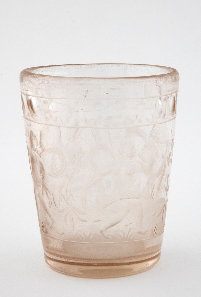 Tilnærmet sylindrisk beger i tykt klart glass med svakt koniske vegger. Yttersiden er dekorert med sliping og gravering. Øverst er det fremstilt en frise med sirkler. Deretter følger fremstillinger av fire nakne barneskikkelser - omgitt av flagrende drapperier og planter - som spiller på ulike musikkinstrumenter.