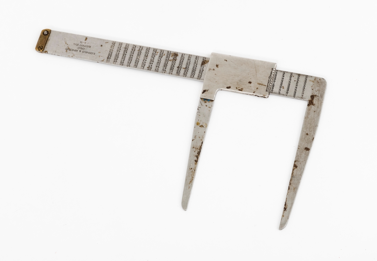 Skyveklave for diameter- og prisberegning av tømmer, altså en såkalt «prisklave». Redskapet er lagd av rustfritt stål. Klaven har en 40,5 centimeter lang, rett linjal med rektangulært tverrsnitt (3,6 X 0,3 centimeter). I den ene enden er det en rettvinklet 17,5 centimeter lang klavearm (målt langs innersida, 21,3 centimeter utvendig) som smalner noe mot ytterenden. Klaven har også en bevegelig arm med samme lengde og samme vinkling i forhold til linjalaksen. Denne armen er festet til en 8,9 centimeter lang fal, ei stålhylse, som omslutter klavelinjalen og tjente som handtak når den bevegelige klavearmen skulle posisjoneres under målingsarbeidet. Denne komponenten hindres fra å løsne ved hjelp av et påklinket messingbeslag i ytterenden av klavelinjalen. På begge sider av ståldekselet er tallene 6, 7, 8, 9, 10, 11, 12, 13, 14, 15 og 16 innstemplet. Disse tallene refererer antakelig til relevante lengdemål på tømmerstokker, oppgitt i halvmetere. Ved å sammenholde disse tallene med tallrekker på klavelinjalens plansider kunne man lese grunnprisinformasjon i hele kronebeløp. Over den ene av disse tabellene, mot linjalkanten, finner vi også ei tallrekke som gjorde det mulig å lese av stokkdiametere mellom 8 og 35 centimeter. Den ytre delen av linjalen er stempelmerket «BJØRNRUD & ARNESTAD  OSLO  RUSTFRITT STÅL  6-16». På den ene sida av stålfalen for den bevegelige klavearmen har noen risset inn tallet «30». Dette kan ha vært et nummer som refererte til Sønsterud skogskoles lister over materiell som ble stilt til elevenes disposisjon i forbindelse med praksisundervisninga.