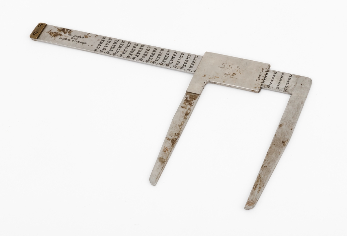 Skyveklave for diameter- og prisberegning av tømmer, altså en såkalt «prisklave». Redskapet er lagd av rustfritt stål. Klaven har en 40,5 centimeter lang, rett linjal med rektangulært tverrsnitt (3,1 X 0,3 centimeter). I den ene enden er det en rettvinklet 17,5 centimeter lang klavearm (målt langs innersida, 20,7 centimeter utvendig) som smalner noe mot ytterenden. Klaven har også en bevegelig arm med samme lengde og samme vinkling i forhold til linjalaksen. Denne armen er festet til en 9,0 centimeter lang fal, ei stålhylse, som omslutter klavelinjalen og tjente som handtak når den bevegelige klavearmen skulle posisjoneres under målingsarbeidet. Denne komponenten hindres fra å løsne ved hjelp av et påklinket messingbeslag i ytterenden av klavelinjalen. På den ene sida av stålhylsa, ved kanten, er tallene 6, 7, 8, 9 innstemplet, på den andre sida fortsetter tallrekka med 11, 12, 13, 14, 15 og 16. Disse sifrene refererer antakelig til relevante lengdemål på tømmerstokker, oppgitt i halvmetere. Ved å sammenholde disse tallene med tallrekker på klavelinjalens plansider kunne man lese grunnprisinformasjon i hele kronebeløp. Over den ene av disse tabellene, mot linjalkanten, finner vi også ei tallrekke som gjorde det mulig å lese av stokkdiametere mellom 8 og 35 centimeter. Den ytre delen av linjalen er stempelmerket «BJØRNRUD & ARNESTAD  OSLO  RUSTFRITT STÅL  6-16». På den ene sida av stålfalen for den bevegelige klavearmen har noen risset inn bokstav- og tallkonstellasjonen «S.S.S. 48». Bokstavene er nok en forkortelse for Statens skogskole Sønsterud. Tallene kan ha vært et nummer som refererte til skogskoles lister over materiell som ble stilt til elevenes disposisjon i forbindelse med praksisundervisninga.