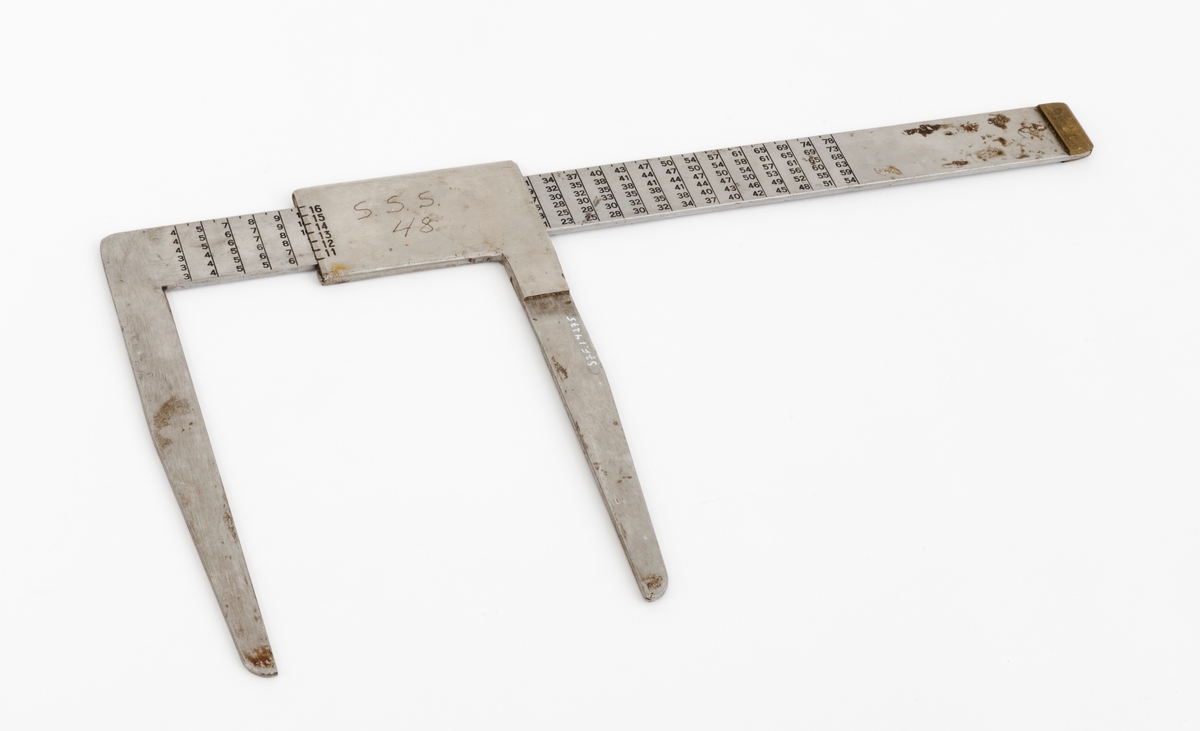 Skyveklave for diameter- og prisberegning av tømmer, altså en såkalt «prisklave». Redskapet er lagd av rustfritt stål. Klaven har en 40,5 centimeter lang, rett linjal med rektangulært tverrsnitt (3,1 X 0,3 centimeter). I den ene enden er det en rettvinklet 17,5 centimeter lang klavearm (målt langs innersida, 20,7 centimeter utvendig) som smalner noe mot ytterenden. Klaven har også en bevegelig arm med samme lengde og samme vinkling i forhold til linjalaksen. Denne armen er festet til en 9,0 centimeter lang fal, ei stålhylse, som omslutter klavelinjalen og tjente som handtak når den bevegelige klavearmen skulle posisjoneres under målingsarbeidet. Denne komponenten hindres fra å løsne ved hjelp av et påklinket messingbeslag i ytterenden av klavelinjalen. På den ene sida av stålhylsa, ved kanten, er tallene 6, 7, 8, 9 innstemplet, på den andre sida fortsetter tallrekka med 11, 12, 13, 14, 15 og 16. Disse sifrene refererer antakelig til relevante lengdemål på tømmerstokker, oppgitt i halvmetere. Ved å sammenholde disse tallene med tallrekker på klavelinjalens plansider kunne man lese grunnprisinformasjon i hele kronebeløp. Over den ene av disse tabellene, mot linjalkanten, finner vi også ei tallrekke som gjorde det mulig å lese av stokkdiametere mellom 8 og 35 centimeter. Den ytre delen av linjalen er stempelmerket «BJØRNRUD & ARNESTAD  OSLO  RUSTFRITT STÅL  6-16». På den ene sida av stålfalen for den bevegelige klavearmen har noen risset inn bokstav- og tallkonstellasjonen «S.S.S. 48». Bokstavene er nok en forkortelse for Statens skogskole Sønsterud. Tallene kan ha vært et nummer som refererte til skogskoles lister over materiell som ble stilt til elevenes disposisjon i forbindelse med praksisundervisninga.