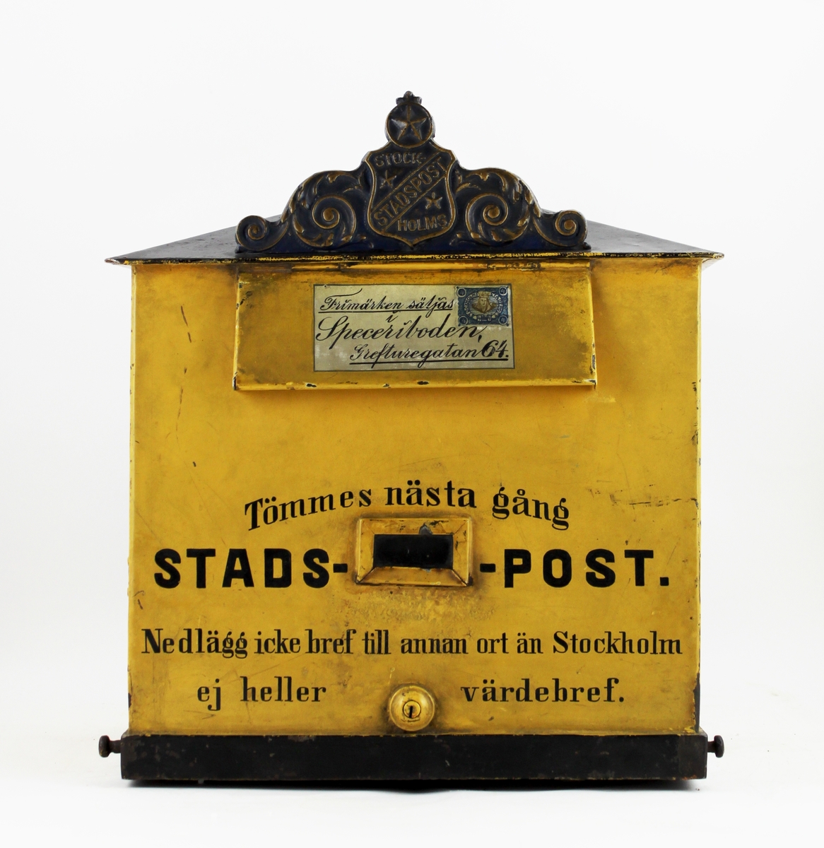 Brevlåda med sluttande, brutet tak. I främre delen av taket ett av Stockholms stadspost emblem. Brevlådans tak och ramen runt brevlådans botten är svart i övrigt är brevlådan gul. På inläggsklaffen ett vitt kuvert med ett av Stadspostens frimärken och texten "Frimärken säljas i Speceriboden Grefturegatan 64".
Där under en liten glasruta avsedd för visning av tömningstider. Brevlådans front har inskription. Brevlådan tömmes från botten med en tömningsväska. Ett lås är centrerat i lådans nederkant. Nyckeln har PM 1642.