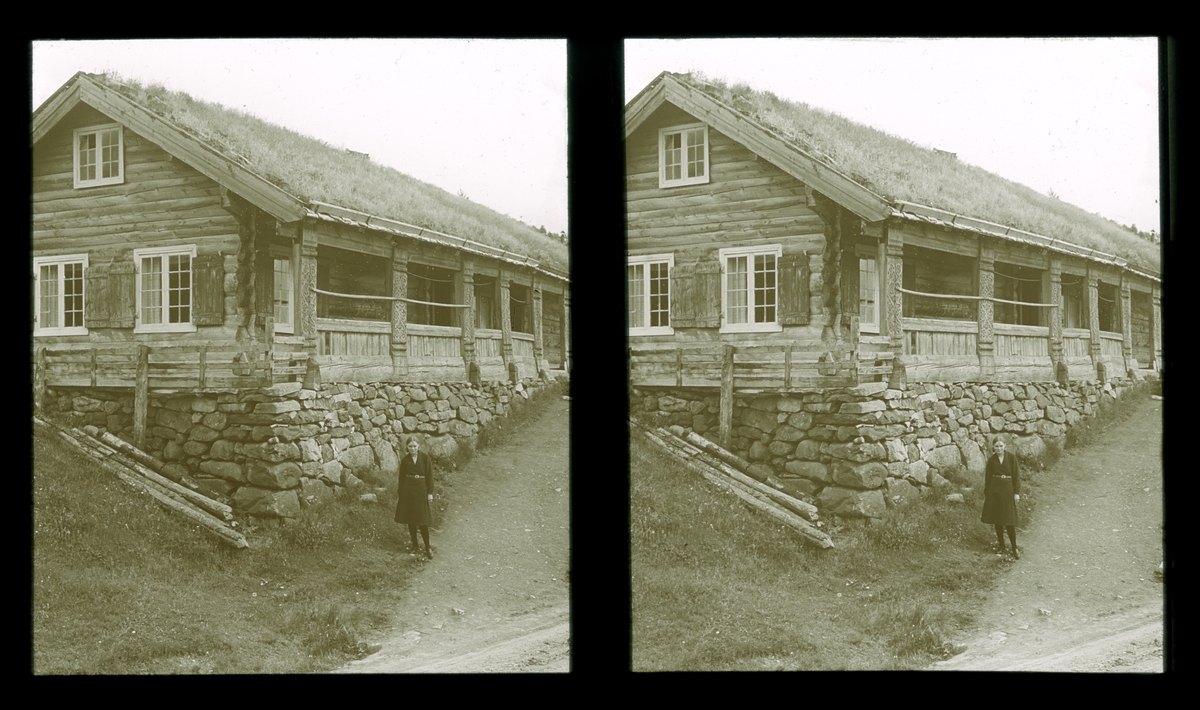 Ung kvinne foran et laftet tømmerhus. Tilhører Arkitekt Hans Grendahls samling av stereobilder.