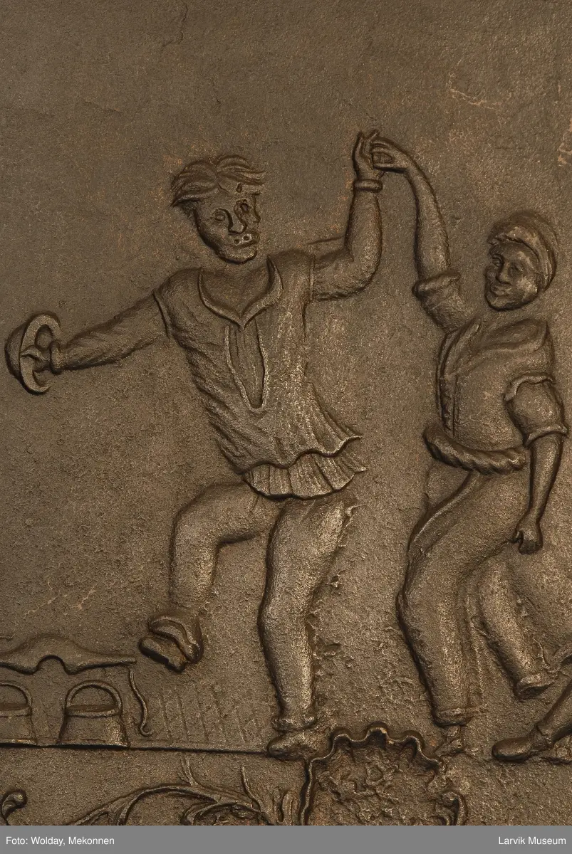 dansende bønder til høyre spillemann med sekkepipe sittende i profil mot venstre på lav krakk til venstre vassele og to trebøtter.