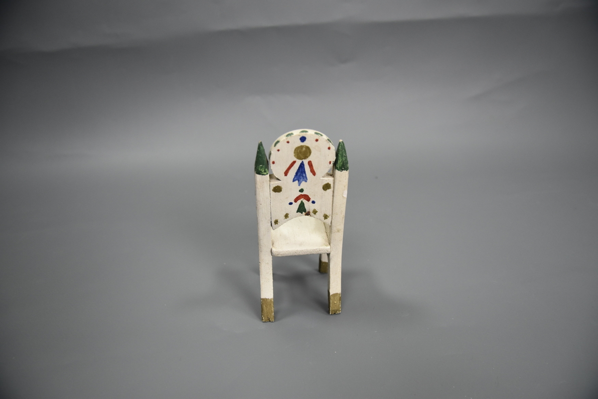 Stol til dokkemøblement i fem deler. Denne stolen er litt mindre enn de tre andre. Møblene er hvitmalte med dekor i ulike farger. 
Møblementet er fra givers tidlige barndom, muligens 1928-1930. Møblene var til hennes første dokkestue, bygget av far av en appelsinkasse. 