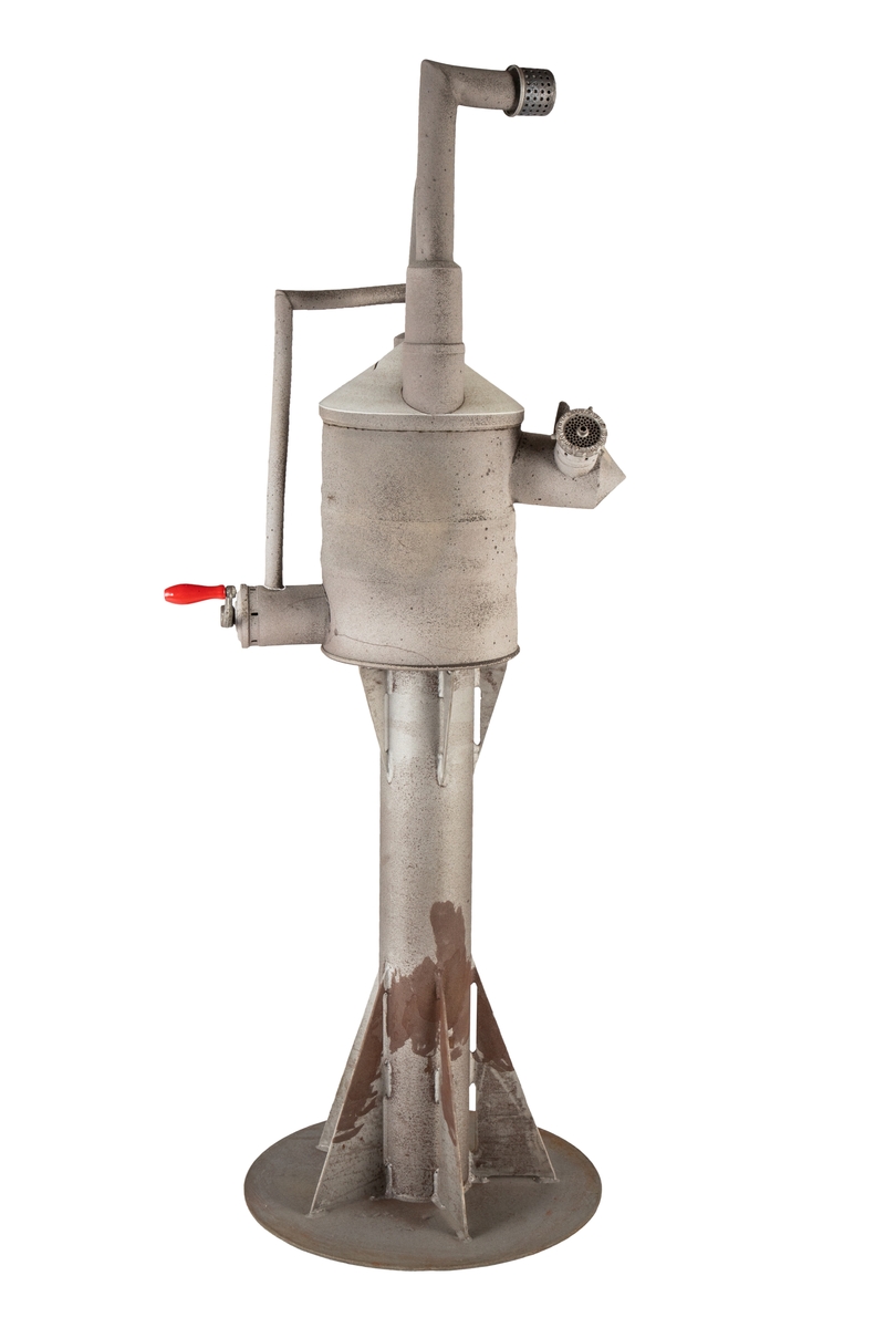 Keramisk skulptur på søylesokkel av jern. Metallet og keramikken er behandlet for å ha lik farge og tekstur; skulpturen mimer også funksjonelle maskindeler fra industrien, med rør, piper, ventil og sveiv. Den høyreiste skulpturen har samtidig et en-til-en forhold til menneskekroppen, og får dermed et figuraktig uttrykk. Den har arkitektoniske trekk fra vanntårn, slik tittelen hentyder, men her skjer i så fall driften skranglete og manuelt på utsiden. Basen har en sirkulær fot, en sylindrisk søyle med trekantede forsterkninger ned mot foten og opp mot topplaten, som er tilsvarende sirkulær, men med mindre diameter enn foten. Keramikkskulpturen består av en sylindrisk beholder, men med utstikkere både til to sider og opp fra et konisk topplokk. Alle utstikkerne er inspirert av maskindeler, og deres visuelle uttrykk refererer til en funksjon snarere enn å faktisk inneha noen funksjon (rørene er dermed ikke rør og sveiven ingen roterbar sveiv - selv om de i det følgende beskrives slik). Ut fra sylinderens ene side er det en metallsveiv med et rødt trehåndtak, og fra den andre siden en utstikker med to åpninger - den ene av disse har et integrert lokk med små hull og bokstaver på rammen (HUSQVARNA SVERIGE V.F.A.B. - et kjapt nettsøk gir en rekke treff på kjøttkvern, som også kan være opphavet til metallsveiven med trehåndtak). Utstikkerne oppover er to rør med forgreininger til hverandre og til et tredje, smalere rør som er ført ned til sveivefunksjonen. Det høyeste røret går vertikalt før det vinkles 90 grader, og avsluttes med en hette med små perforeringer på tuppen.