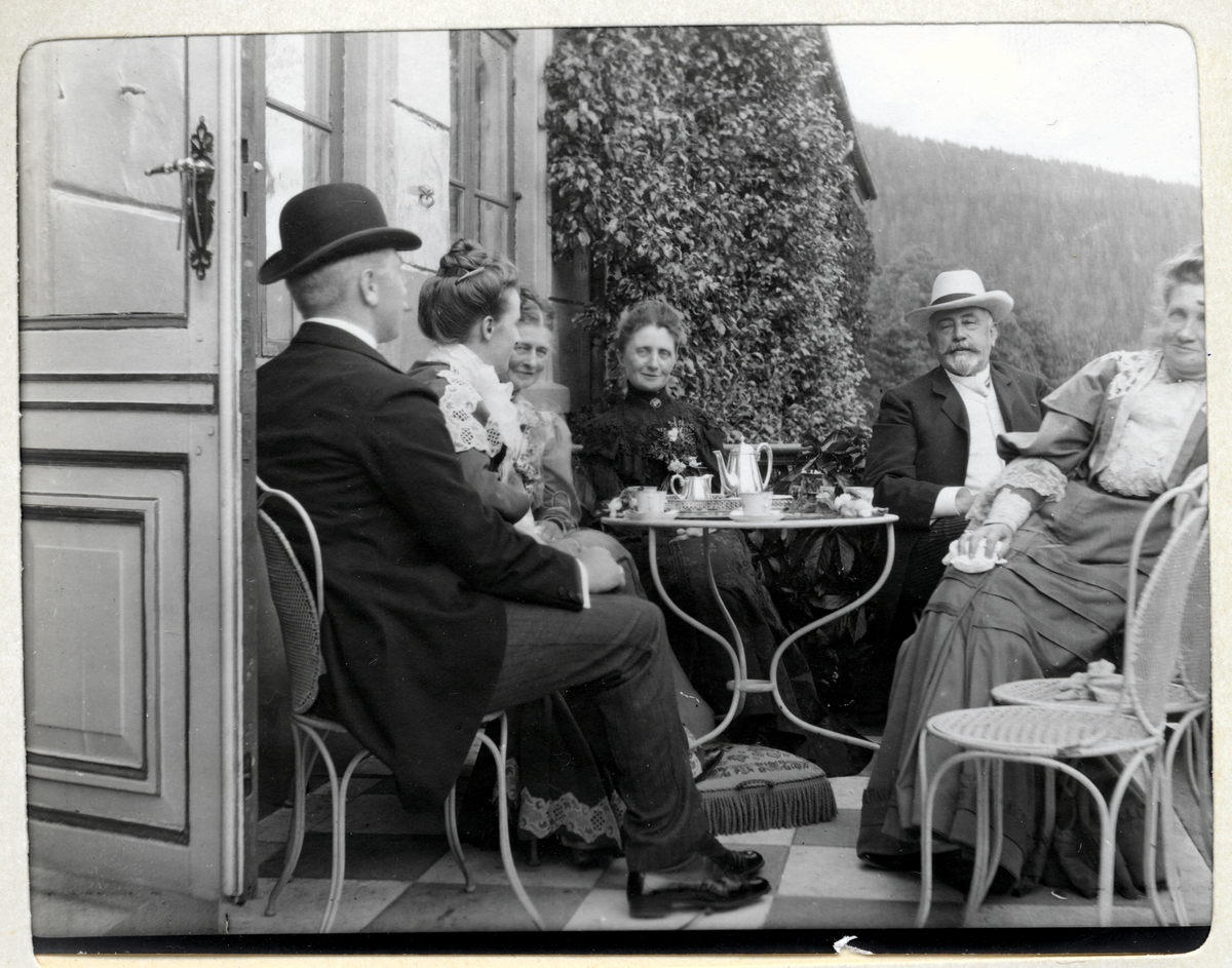 Fire kvinner og to menn drikker kaffe på verandaen på Bogstad gård. Til venstre Westye Egeberg og Nini Egeberg. I midten antagelig Ninis foreldre, Mathilde og Herman Wedel Jarlsberg. Fotografert 7. juli 1905.