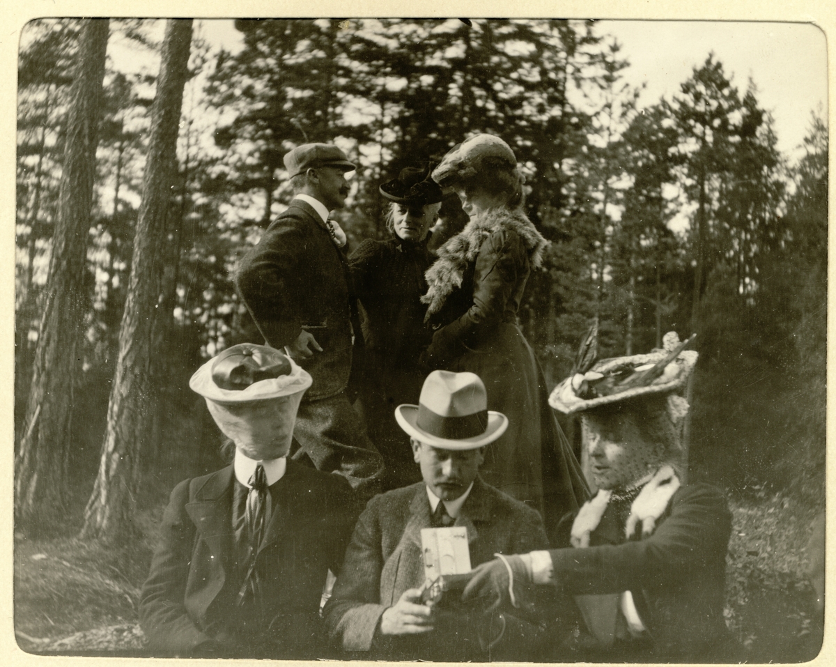 Elgjegere med følge holder pause under jakten på Fossum gård i Bærum(?). Kvinnene bærer hatter med slør som beskyttelse mot insekter. Fotografert september 1905.