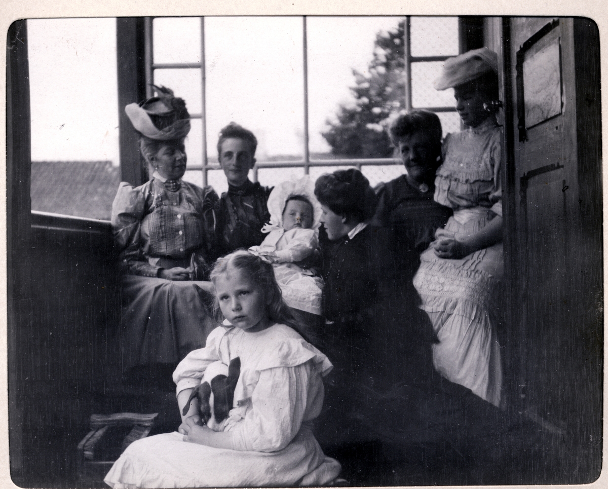 Fire kvinner og to barn på veranda på Strøm gård, antagelig Vestre Strøm gård i Rælingen. Nummer to til venstre er antagelig Nini Egeberg med datteren Mimi på fanget. Fotografert august 1906.