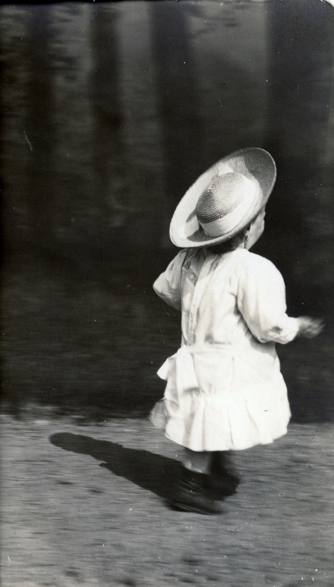 Lille Mimi Egeberg spaserer i parken på Bogstad gård, iført kjole og hatt. Fotografert 1907.